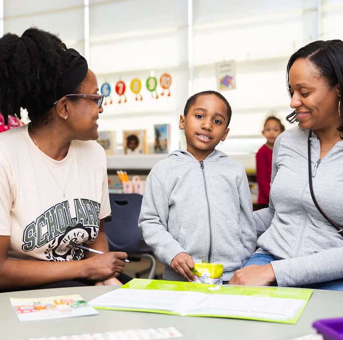 A young child sitting in between two women in a classroom setting